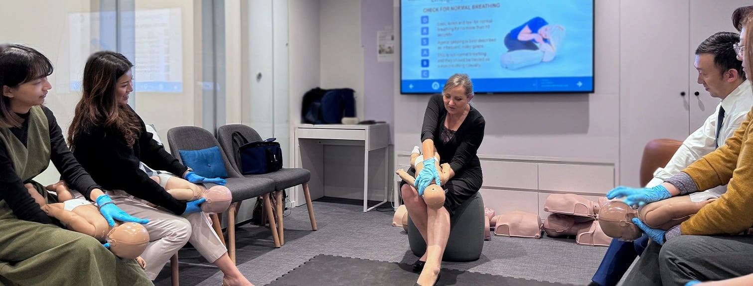 An adult performing breathing check on a dummy child in a classroom